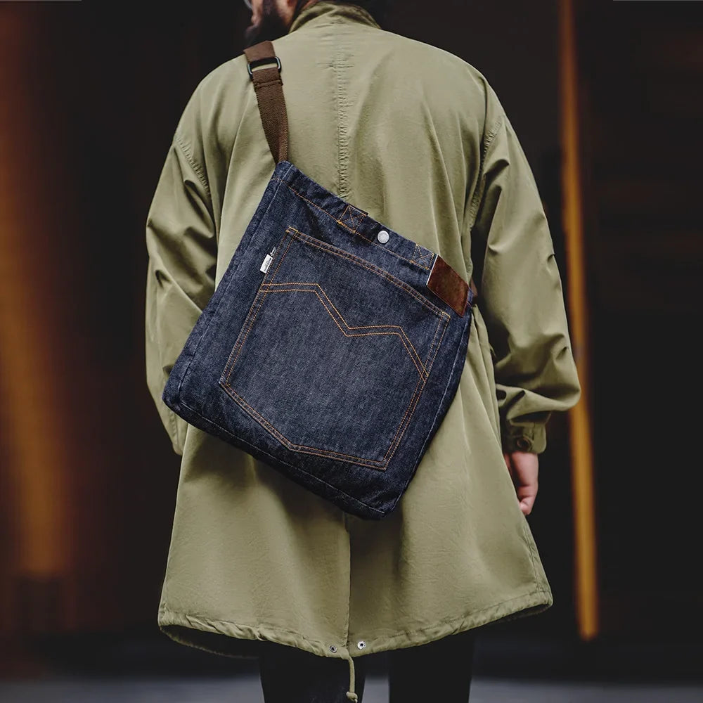 Man wearing the navy denim tote bag crossbody over an olive coat, brown adjustable strap across his back