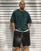 Man in green tee and black mesh shorts by metal shutter — front