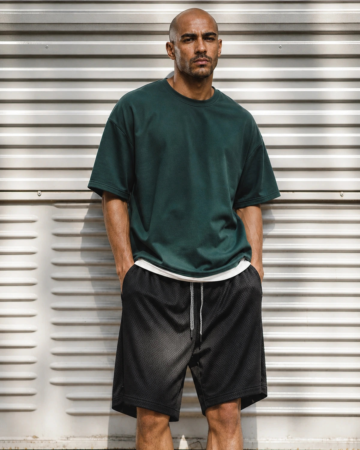 Man in green tee and black mesh shorts by metal shutter — front