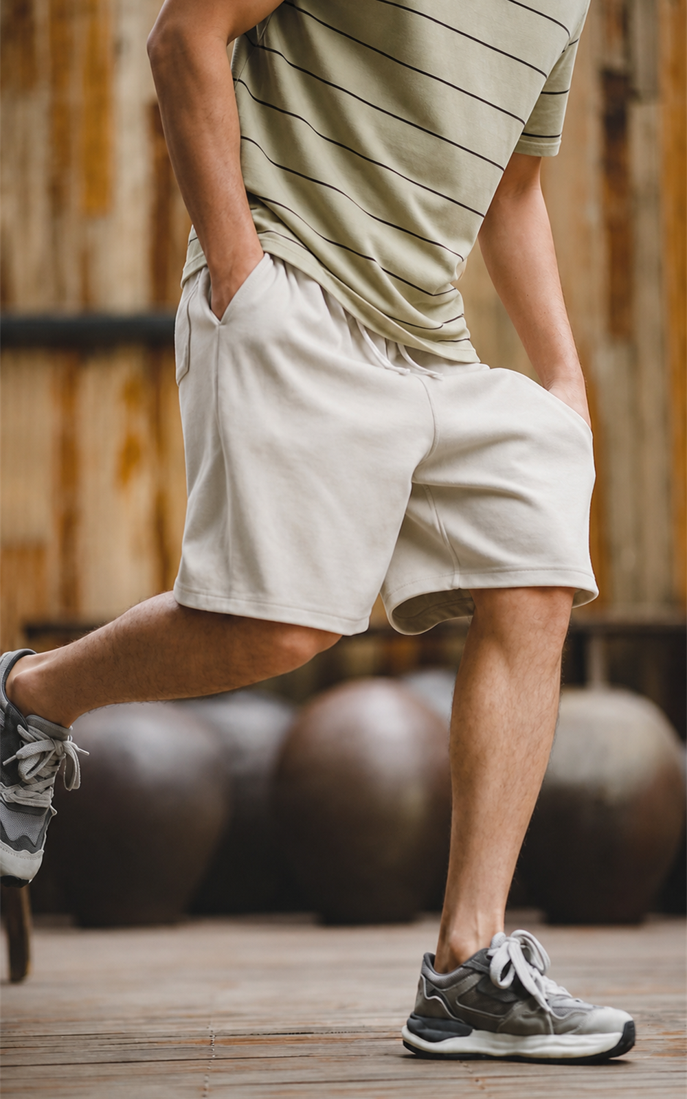 Man in striped tee stepping forward in cream knit shorts on wooden deck