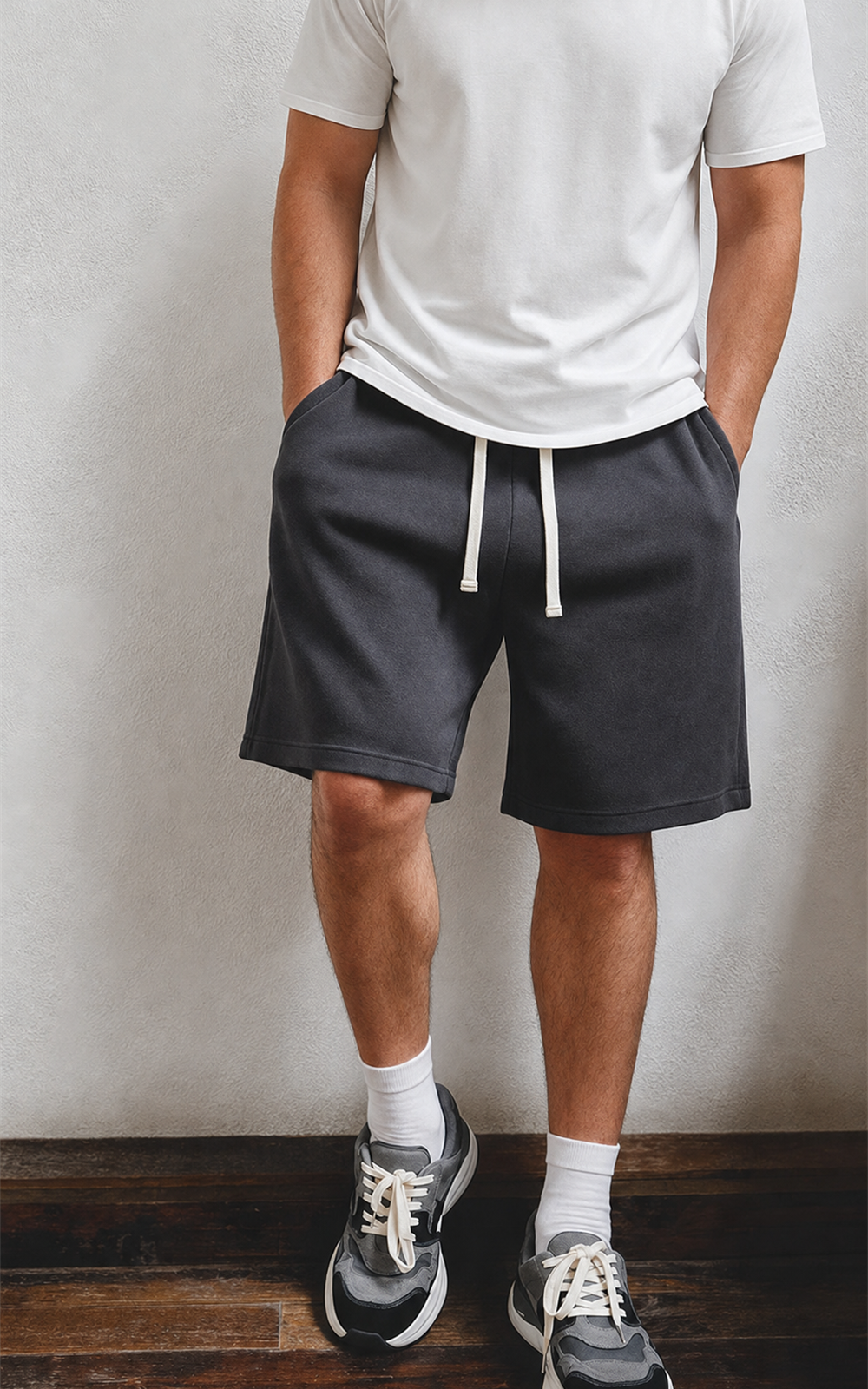 Man in white tee wearing washed charcoal knit shorts against wall