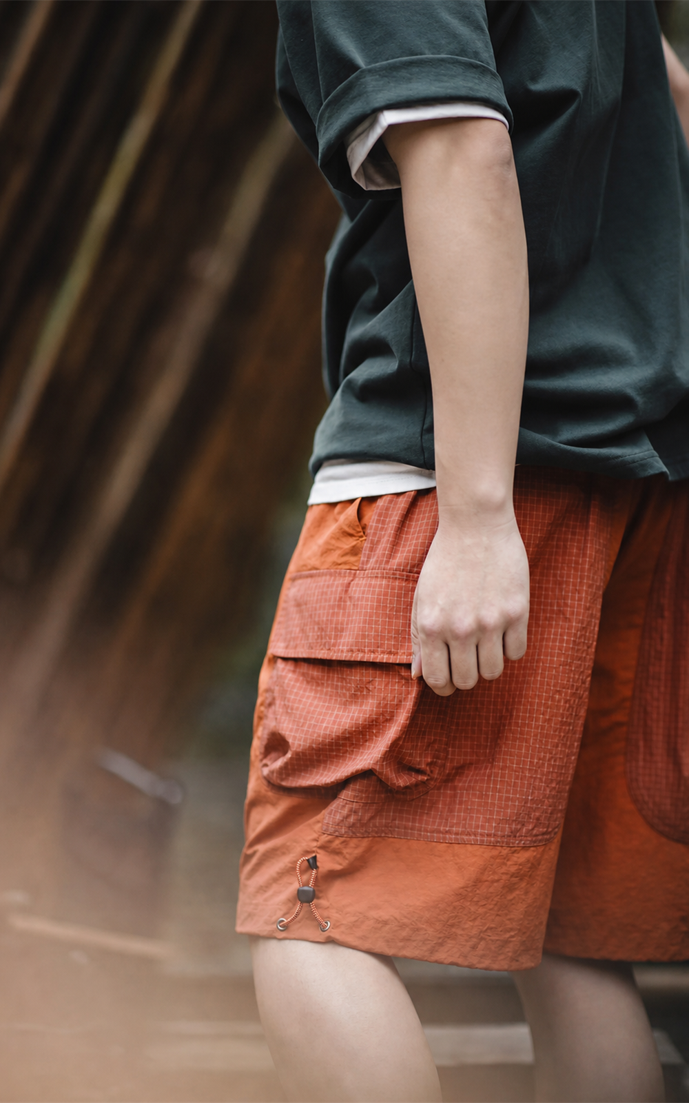 Gingham-texture patch pocket and hem toggle on orange shorts — close-up