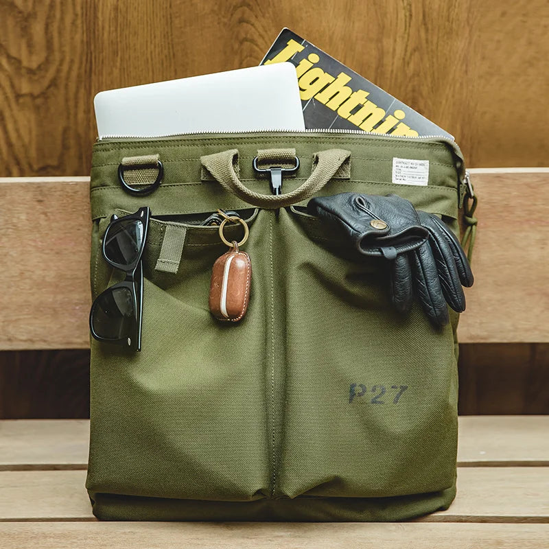 Military Green helmet messenger bag held by the top handles, showing twin front patch pockets