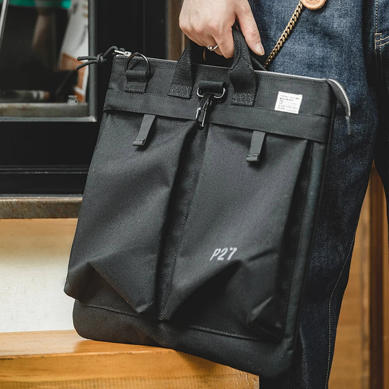 Man carrying the charcoal helmet messenger bag by its top handles, P27 stencil on the front panel
