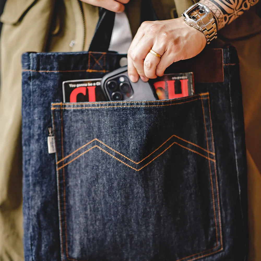Hand sliding a phone into the front patch pocket of the navy denim tote bag
