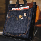 Navy 14oz denim tote bag standing upright, showing the large front patch pocket with orange chevron stitching