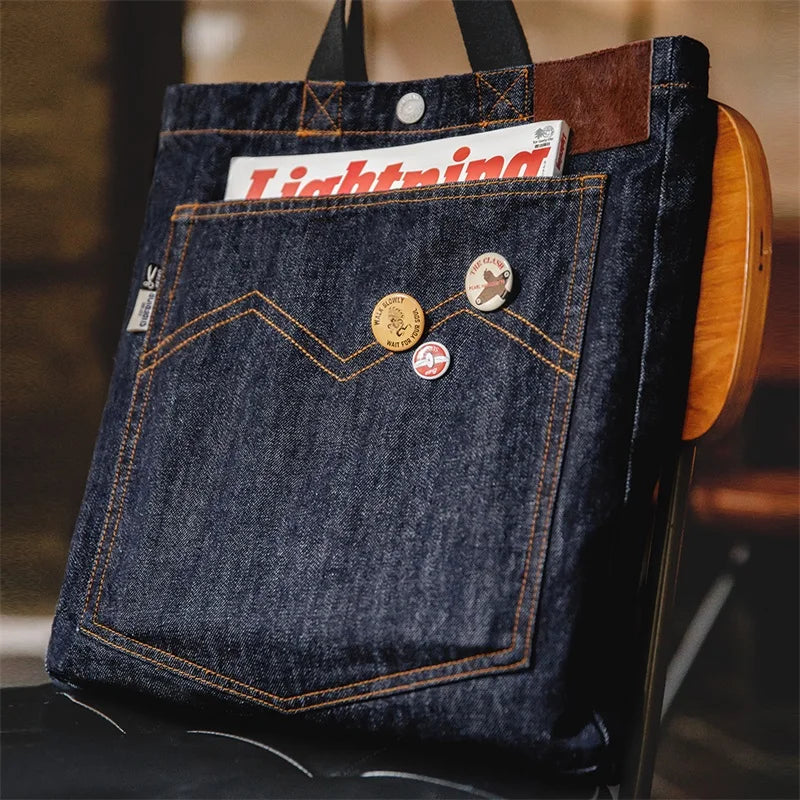 Navy 14oz denim tote bag standing upright, showing the large front patch pocket with orange chevron stitching