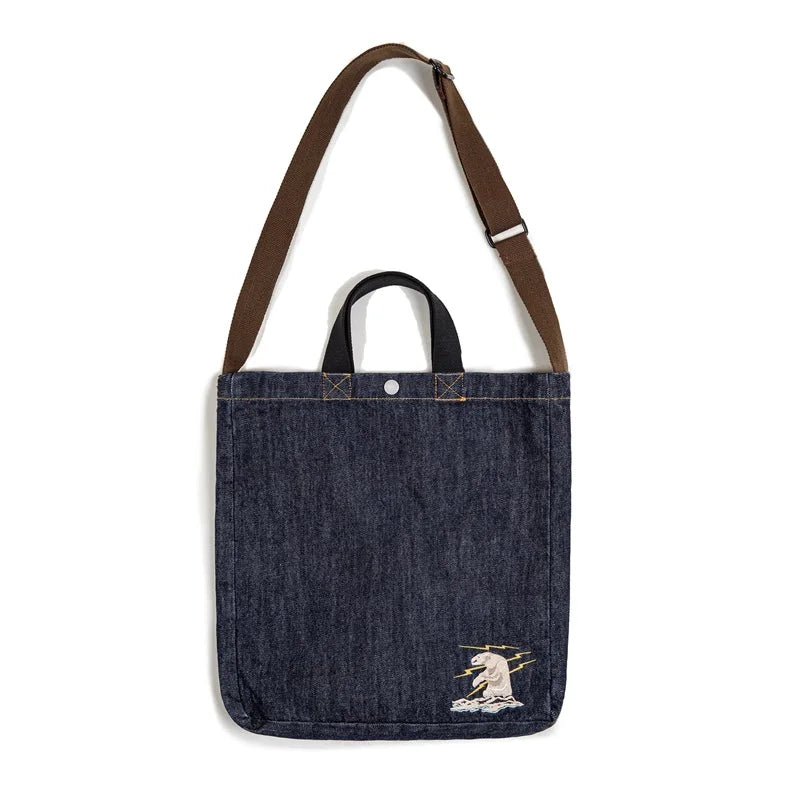 Navy denim tote bag on a white background with the brown shoulder strap extended to full length