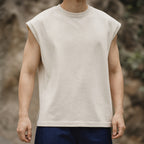 Man wearing the beige boxy sleeveless knit vest with blue trousers