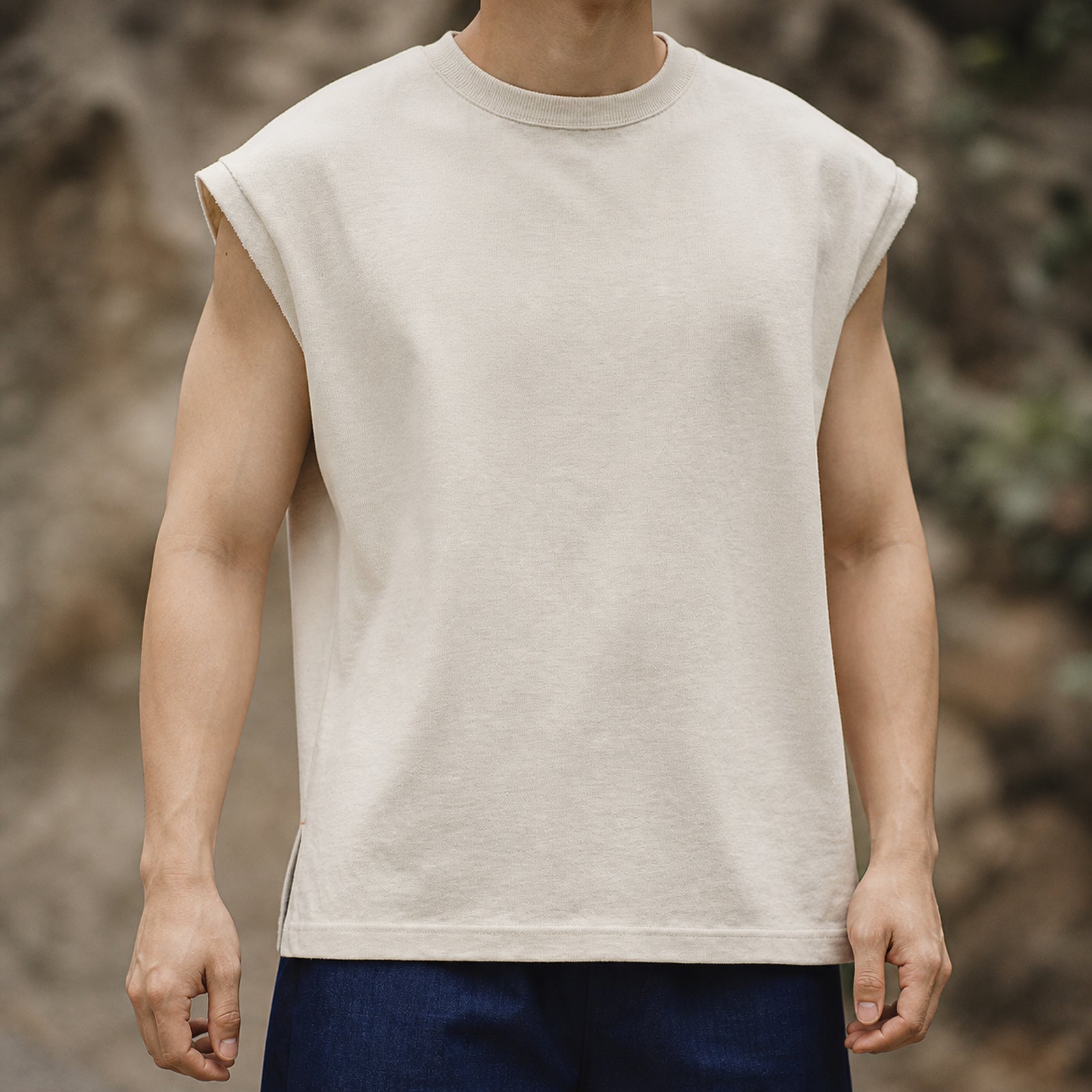 Man wearing the beige boxy sleeveless knit vest with blue trousers