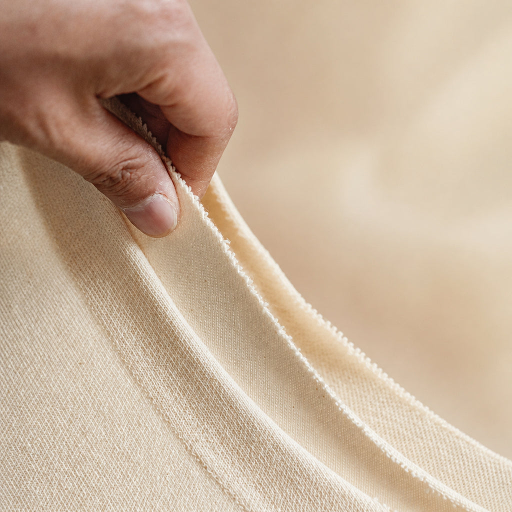 Hand showing the thickness of the beige knitted cotton fabric