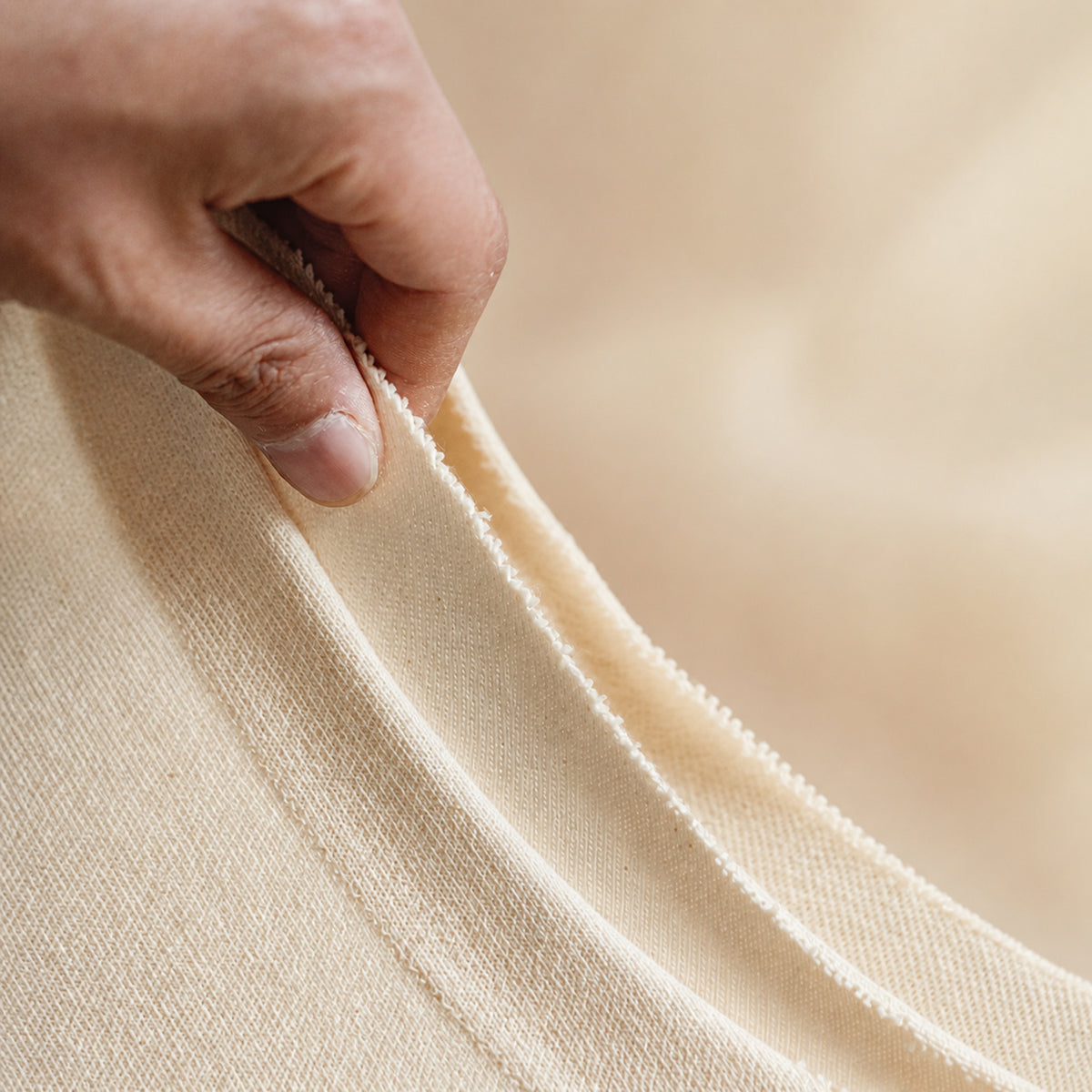 Hand showing the thickness of the beige knitted cotton fabric