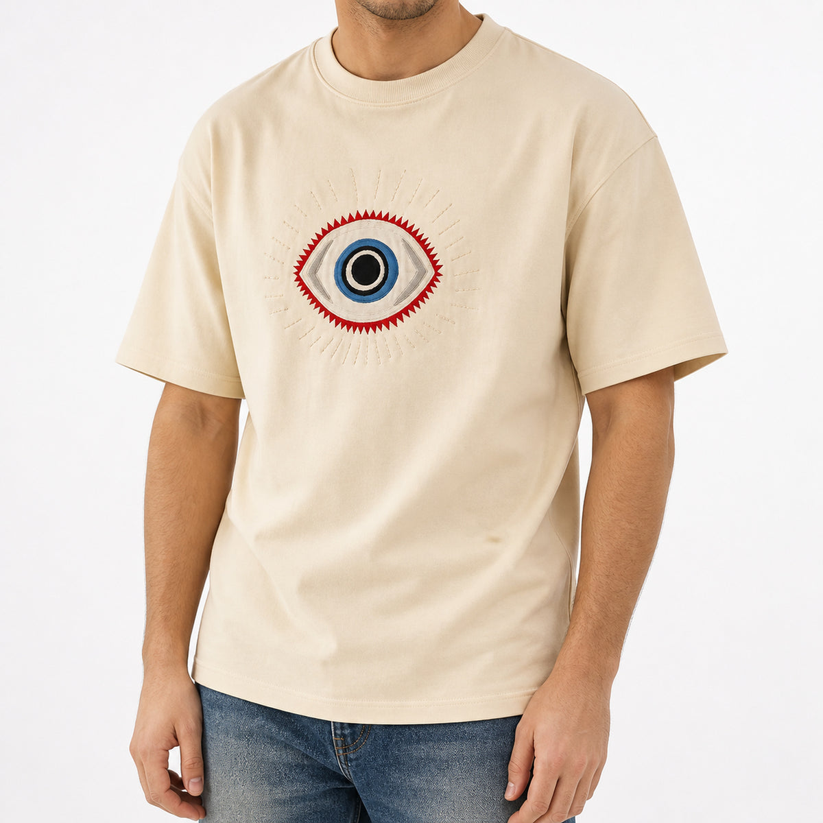 Man wearing the beige guardian eye embroidered t-shirt with blue jeans