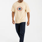 Man wearing the beige guardian eye tee with dark jeans, full view