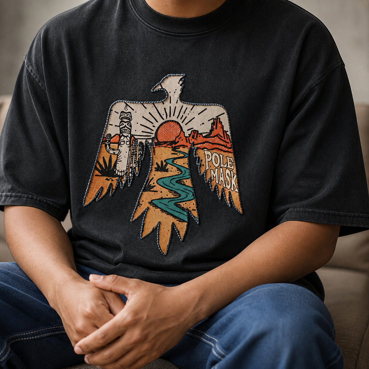 Seated man wearing the washed black thunderbird tee with blue jeans