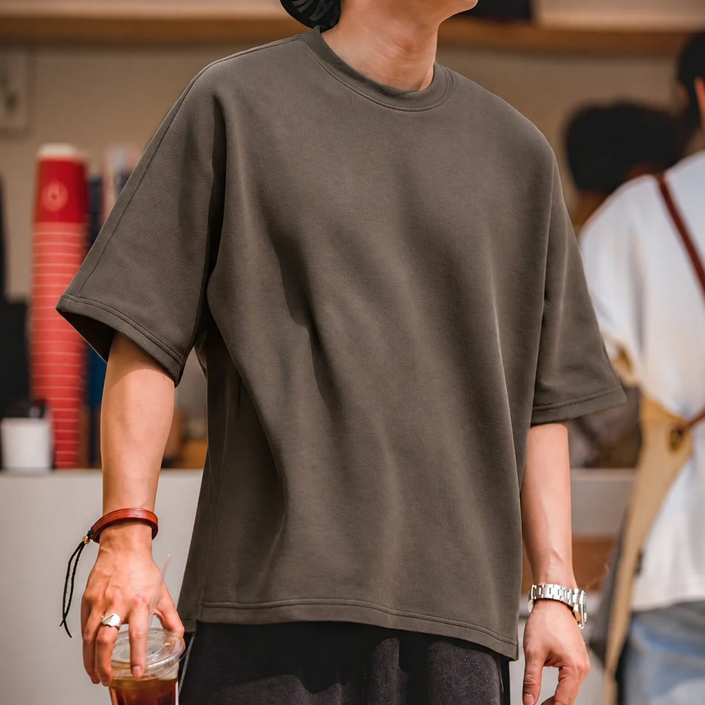 Man in the coffee brown boxy tee holding an iced drink
