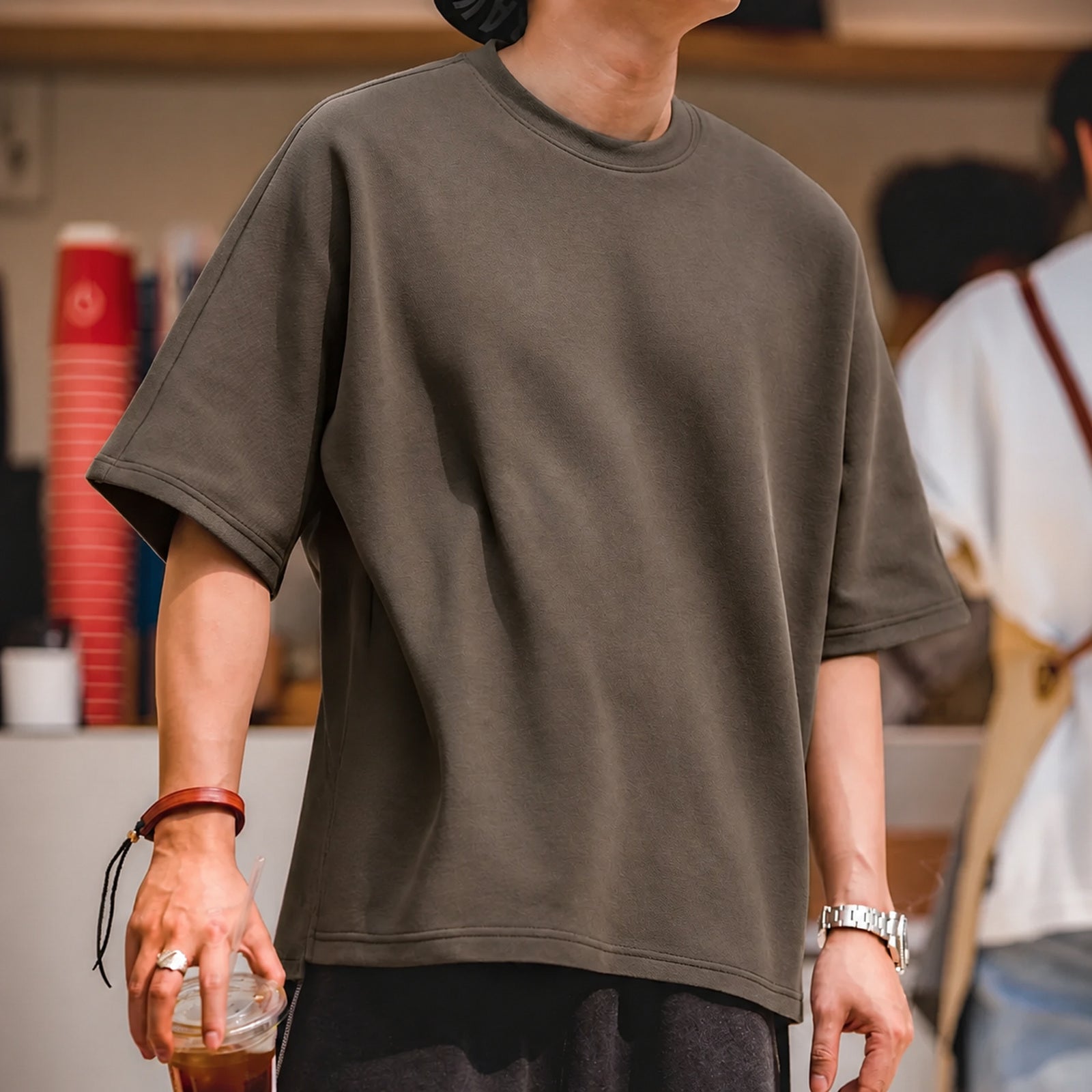 Man in the coffee brown boxy tee holding an iced drink
