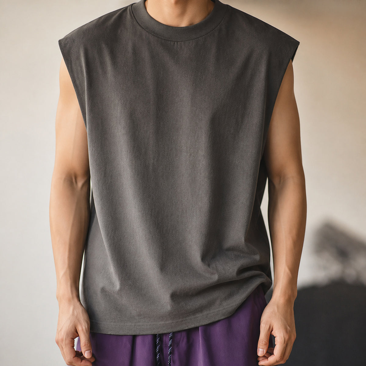 Man in the dark grey boxy sleeveless knit vest, relaxed pose