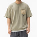 Man wearing the sage green utility tee with contrast crinkle pocket and grey shorts