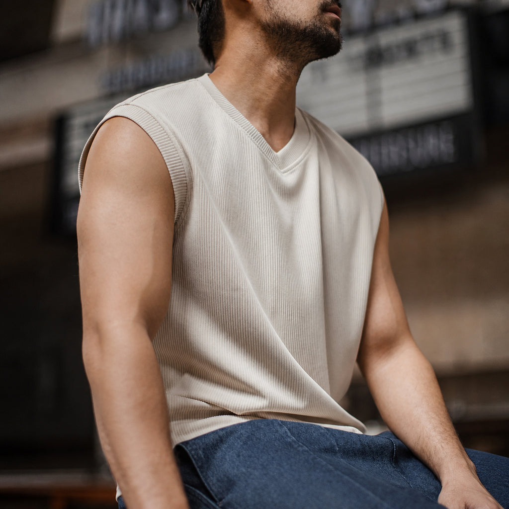 Seated man in the khaki ribbed v-neck tank with blue jeans